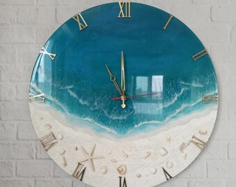 May include: A round clock with a blue and white ocean scene. The clock face has Roman numerals and a gold-colored frame. The ocean scene features a blue wave crashing on a white sandy beach with seashells and a starfish.