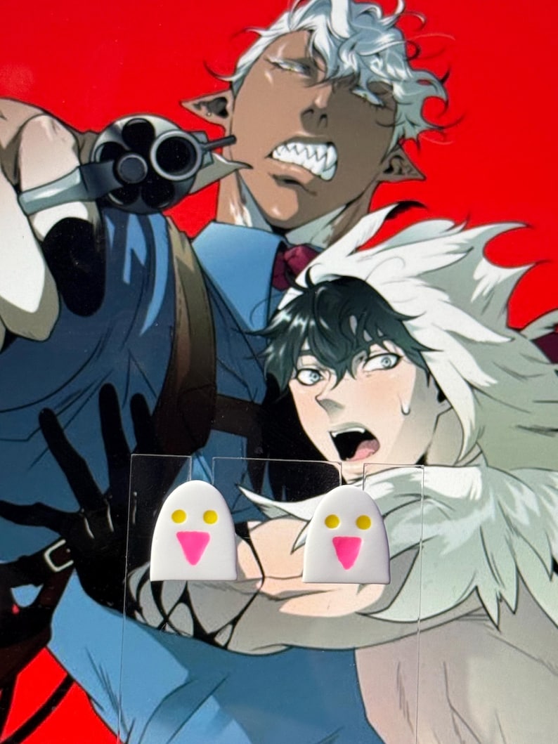 May include: A pair of white stud earrings shaped like ghosts with two yellow circular eyes and a pink triangular mouth, displayed on a clear acrylic card against a background featuring an illustration of two anime characters.