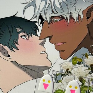 May include: A pair of white ghost-shaped earrings featuring two yellow circular eyes and a pink triangular mouth, displayed on a clear backing card in front of an illustration of two characters with white roses.
