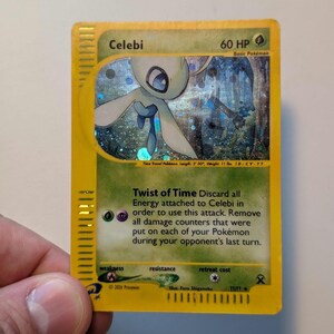 Könnte beinhalten: Eine gelbe Celebi-Pokémon-Karte mit holografischem Hintergrund. Die Karte zeigt ein grünes und weißes Wesen mit dem Text "Celebi" und "60 HP". Die Karte enthält auch den Text "Twist of Time".
