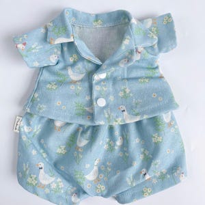 Puede incluir: Un conjunto de mu&ntilde;eca beb&eacute; azul claro con una camisa de manga corta y pantalones cortos. La tela tiene un patr&oacute;n blanco y verde de patos y flores.