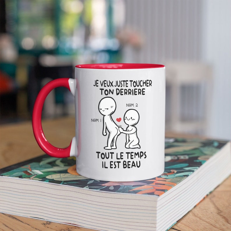 Puede incluir: Taza de cer&aacute;mica blanca con borde y asa rojos. La taza presenta una ilustraci&oacute;n de dibujos animados de dos figuras de palo con el texto "JE VEUX JUSTE TOUCHER TON DERRIERE NOM 1 NOM 2 TOUT LE TEMPS IL EST BEAU".