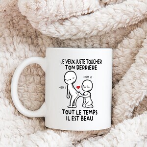 Puede incluir: Taza de cer&aacute;mica blanca con una ilustraci&oacute;n en blanco y negro de dos figuras de palo. El texto en la taza dice "JE VEUX JUSTE TOUCHER TON DERRIERE NOM 1 NOM 2 TOUT LE TEMPS IL EST BEAU".