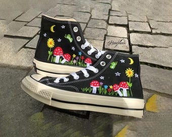 May include: Black high-top canvas shoes with white soles and colorful embroidered mushrooms, stars, and flowers on a black background. The shoes have a white rubber toe cap and a white rubber midsole. The shoes are handmade.