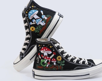 May include: Black high-top canvas sneakers with embroidered mushrooms, stars, and flowers. The shoes have white soles and laces.