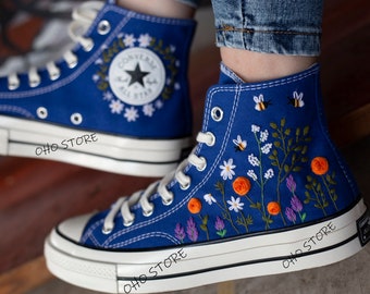 May include: Blue high-top canvas sneakers with white stitching and a white rubber sole. The sneakers are embroidered with a floral design in orange, white, and purple. The text "OHO STORE" is printed on the side of the sneakers.