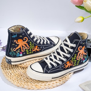 May include: A pair of black canvas high-top trainers with embroidered ocean-themed designs. The trainers feature an orange octopus, blue fish, and green seaweed.