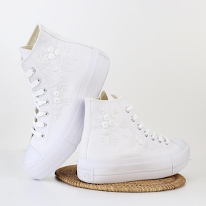May include: White high-top sneakers with delicate floral embroidery and a platform sole.