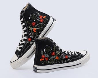 May include: A pair of black high-top canvas sneakers with white soles. The sneakers are embroidered with colorful flowers and greenery.