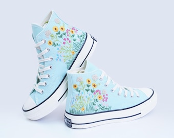 May include: A pair of light blue high-top sneakers with embroidered flowers and green stems. The sneakers have white soles and laces.