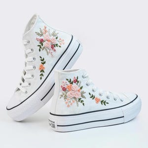 May include: White high-top sneakers with a platform sole and floral embroidery. The embroidery features pink, orange, and green flowers.