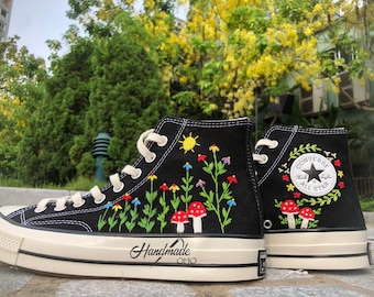 Può includere: Scarpe Converse nere alte con fiori, funghi e un sole ricamati sul lato. Il logo Converse All Star è anche ricamato sul lato. Le scarpe recano la scritta "Handmade Ohio" sul lato.