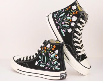 May include: Black high-top Converse sneakers with floral embroidery. The embroidery features colorful flowers and leaves on a black canvas background.