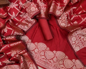 May include: A deep red fabric featuring an intricate woven pattern in a metallic gold tone. The design includes a grid-like structure filled with floral motifs and a wide, ornate border displaying detailed botanical elements and scrolling patterns.