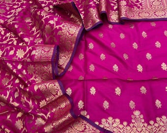 May include: A vibrant magenta fabric featuring intricate gold metallic floral patterns woven throughout. The textile displays a wide decorative border with detailed botanical motifs and a purple hem, complemented by scattered small gold floral sprigs.