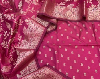 May include: A vibrant magenta fabric featuring an intricate woven pattern in a metallic rose gold tone. The textile displays a dense floral motif across the surface, complemented by a wide, ornate border with detailed botanical designs.