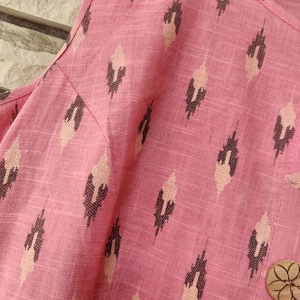 May include: Pink fabric with a geometric pattern of brown and white diamonds. A wooden button with a floral design is visible in the bottom right corner.
