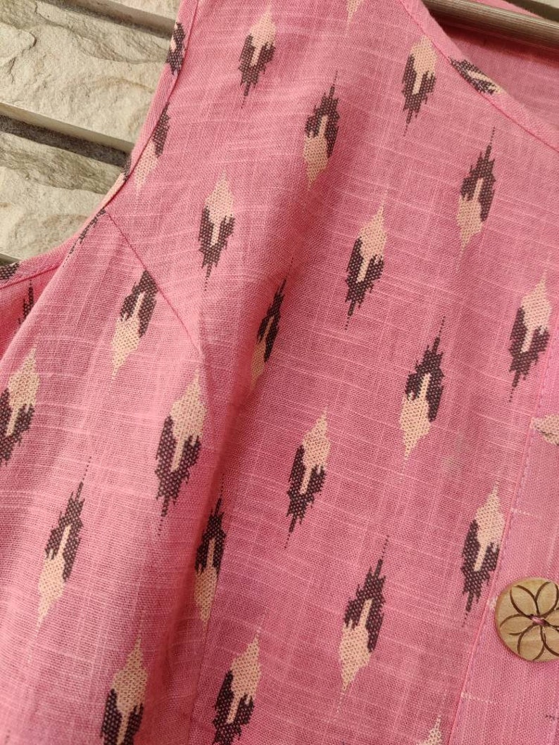 May include: Pink fabric with a geometric pattern of brown and white diamonds. A wooden button with a floral design is visible in the bottom right corner.