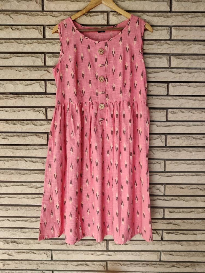 May include: A pink sleeveless dress with a white and black geometric pattern. The dress has a round neckline and a button closure down the front.