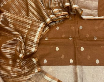 May include: A brown fabric textile featuring a metallic silver striped pattern on the folded section and small, repeating silver teardrop-shaped motifs across the main body, finished with a wide, solid metallic silver border along the edge.
