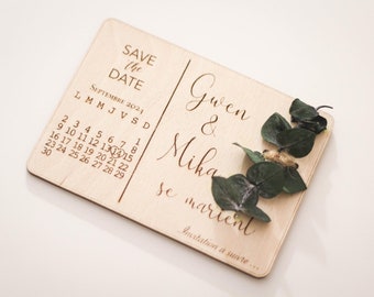 Puede incluir: Una tarjeta de madera de "Save the Date" con un calendario que muestra septiembre de 2021 con un corazón marcando el 14. La tarjeta dice "Gwen & Mika se casan" con una pequeña rama de vegetación.
