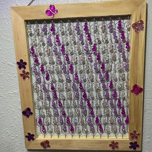 Könnte beinhalten: Ein Holzrahmen mit einem Drahtgitterhintergrund, der mit violetten, rosa und klaren Perlen verziert ist. Der Rahmen ist mit Schmetterlings- und Blumenverzierungen geschmückt.