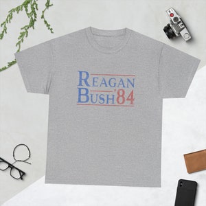 May include: A heather grey t-shirt with the text "Reagan Bush '84" printed in blue and red.