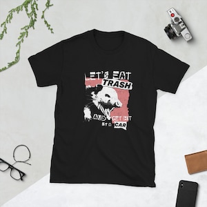 May include: Black t-shirt with a white graphic of a possum with the text "Let's Eat Trash and Get Hit By A Car" in a distressed font.