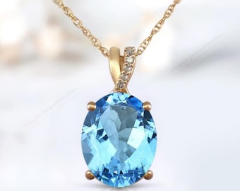 Puede incluir: Un collar de cadena de oro con un colgante que presenta una gran piedra de topacio azul de forma ovalada rodeada de diamantes más pequeños.