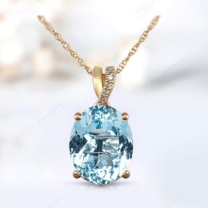 Puede incluir: Un collar de oro con un colgante de piedra ovalada azul claro adornado con pequeños diamantes. El colgante está engastado en una banda de oro retorcida.
