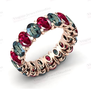 May include: A rose gold eternity band ring with alternating red and green gemstones. The ring is set with oval-shaped stones.