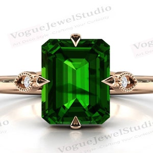 Può includere: Un anello in oro rosa con una grande pietra preziosa verde smeraldo e due piccoli accenti di diamanti. L'anello presenta un design unico in stile Art Deco.