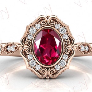 Op de afbeelding: Een verlovingsring in vintage stijl met een grote ovale robijn-edelsteen omringd door een halo van kleinere diamanten. De ring is gezet in roségoud en heeft ingewikkelde kruldetails.