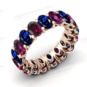 May include: A rose gold eternity band with alternating oval-shaped blue and pink gemstones. The band is set with a continuous row of stones.