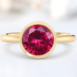 Könnte beinhalten: Ein goldener Ring mit einer Zargenfassung, die einen großen, runden, leuchtend pinkfarbenen Edelstein trägt.