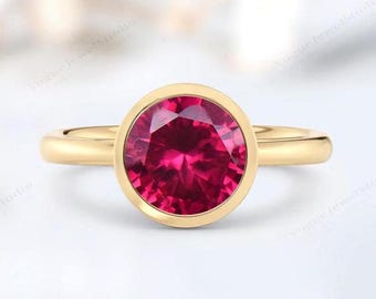 Könnte beinhalten: Ein goldener Ring mit einer Zargenfassung, die einen großen, runden, leuchtend pinkfarbenen Edelstein trägt.