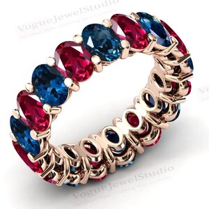 Puede incluir: Un anillo de banda de oro con piedras preciosas ovaladas rojas y azules alternas. El anillo está engastado con una fila continua de piedras preciosas.