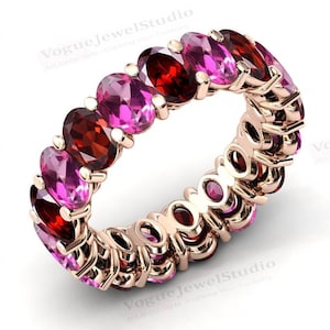 Pode incluir: Uma aliança de eternidade em ouro rosa com gemas ovais rosa e vermelhas alternadas. A aliança é adornada com uma fileira contínua de pedras.