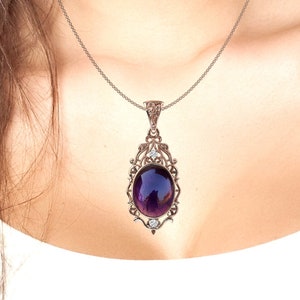 May include: A silver necklace with a purple oval gemstone pendant set in a filigree frame. The pendant has small clear stones on the sides.