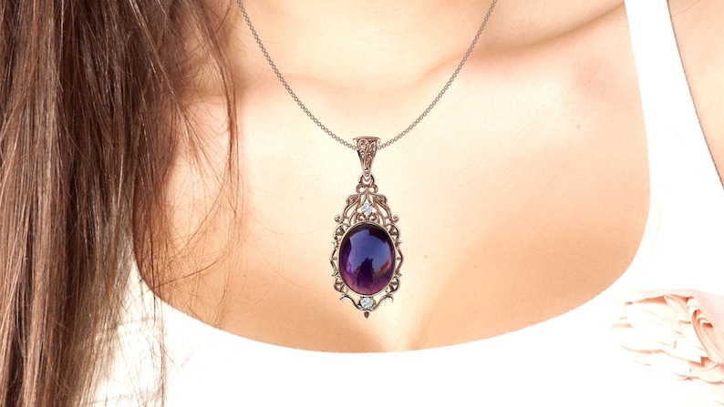 May include: A silver necklace with a purple oval gemstone pendant set in a filigree frame. The pendant has small clear stones on the sides.