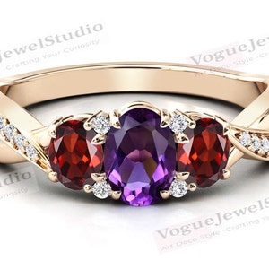 May include: A gold ring with a twisted band set with three oval-shaped gemstones. The center stone is a purple amethyst, and the two side stones are red garnets. The band is also set with small diamonds.