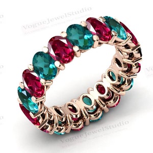 May include: A rose gold eternity band ring with alternating oval-shaped red and green gemstones.