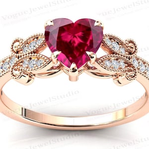 May include: A heart-shaped ruby ring set in rose gold with a delicate butterfly design and small diamonds on the band.