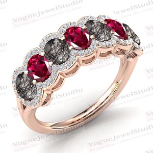 May include: A rose gold ring featuring five oval-cut gemstones. Alternating between vibrant red rubies and black rutilated quartz, each stone is surrounded by a halo of small, sparkling diamonds. The ring's band is a smooth, polished rose gold.