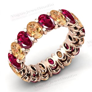 May include: A gold eternity band ring with alternating oval-shaped red rubies and yellow gemstones. The ring is set in a prong setting.
