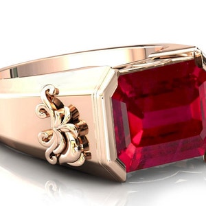 May include: A rose gold ring featuring a large, emerald-cut ruby gemstone. The ring has a decorative, floral design on the side.