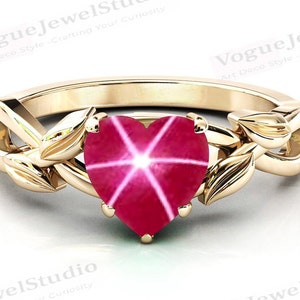 May include: A gold ring featuring a heart-shaped ruby gemstone. The ring has a delicate leaf design on either side of the stone.