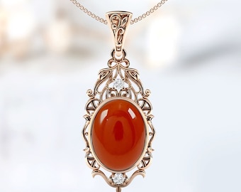 May include: A rose gold pendant necklace featuring a large oval carnelian gemstone set within a filigree design and accented with small clear diamonds.