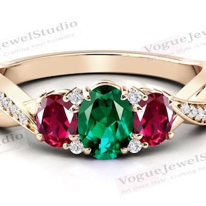 Può includere: Un anello d'oro con una fascia intrecciata incastonata con tre pietre ovali. La pietra centrale è uno smeraldo verde vibrante, affiancato da due pietre rubino rosse. La fascia è decorata con piccoli diamanti trasparenti.