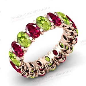 May include: A rose gold eternity band ring with alternating red ruby and green peridot gemstones.